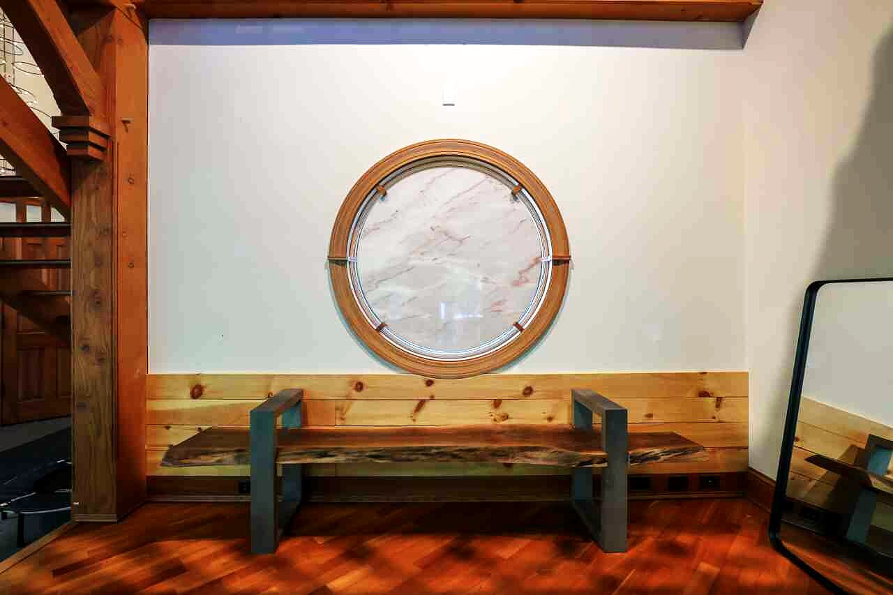 A round porthole window of pink Carnegie marble above a live-edge bench.
