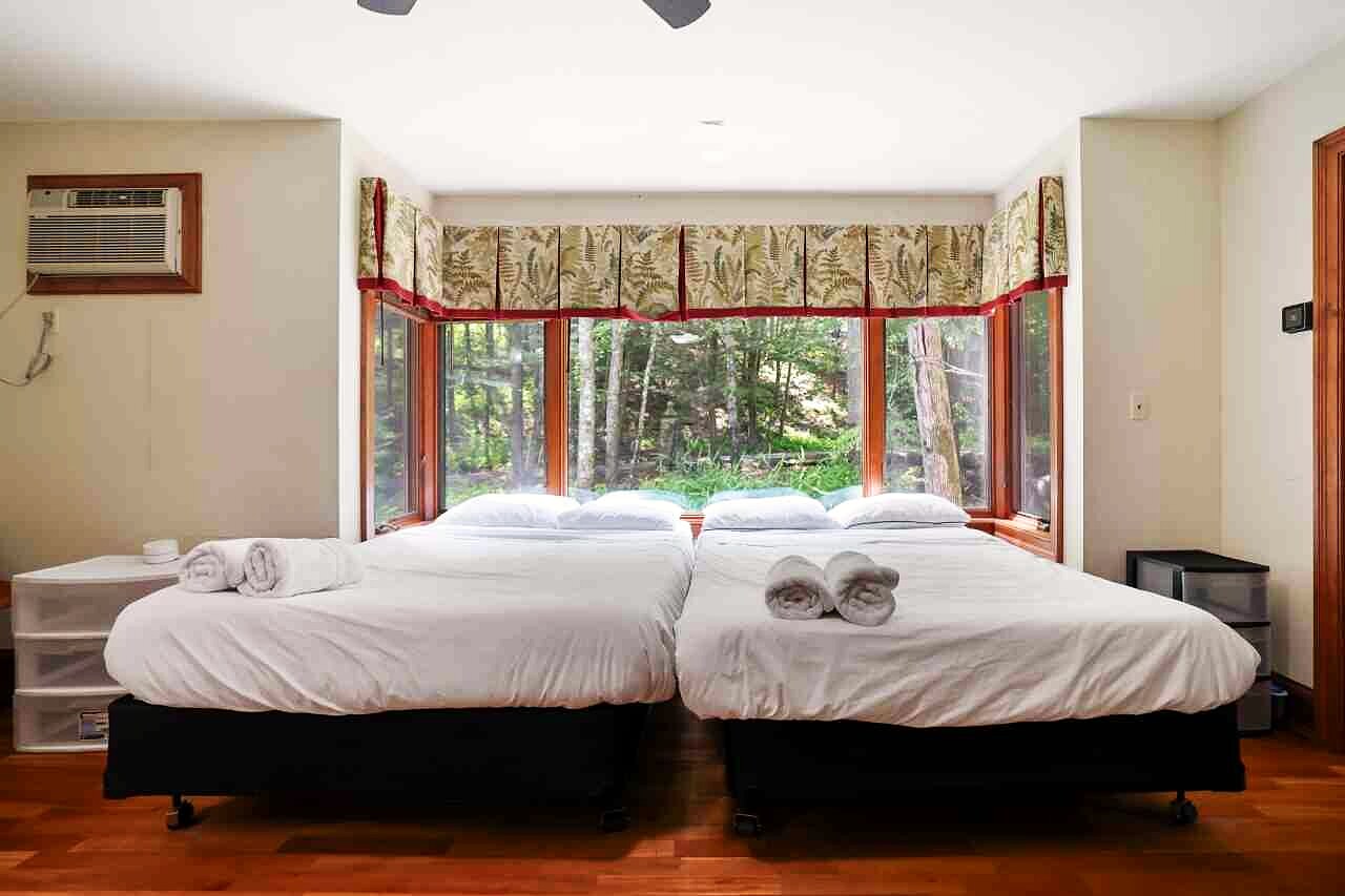 A bedroom with twin beds and a deep bay window onto the forest.