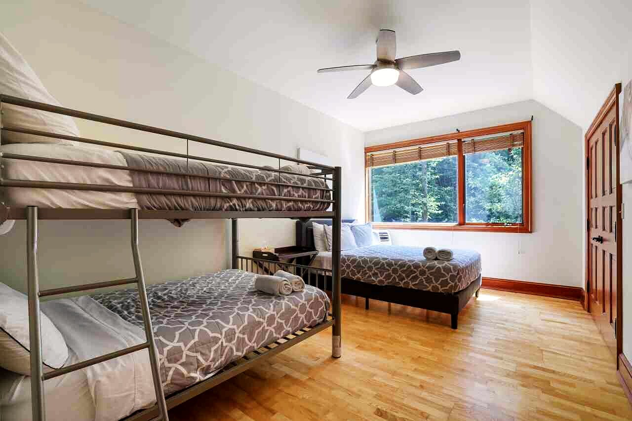 A bedroom under the eaves with a corner of windows and a forest view.